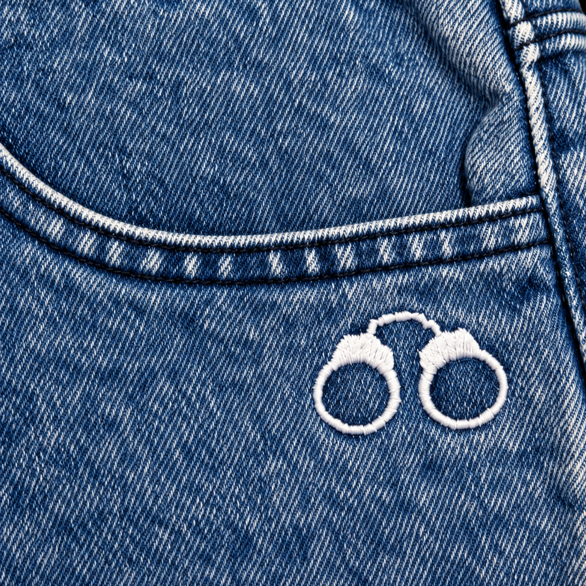 CROOKSLDN Blue Wash Yard Jeans — close-up of white handcuff embroidery below the front pocket seam.