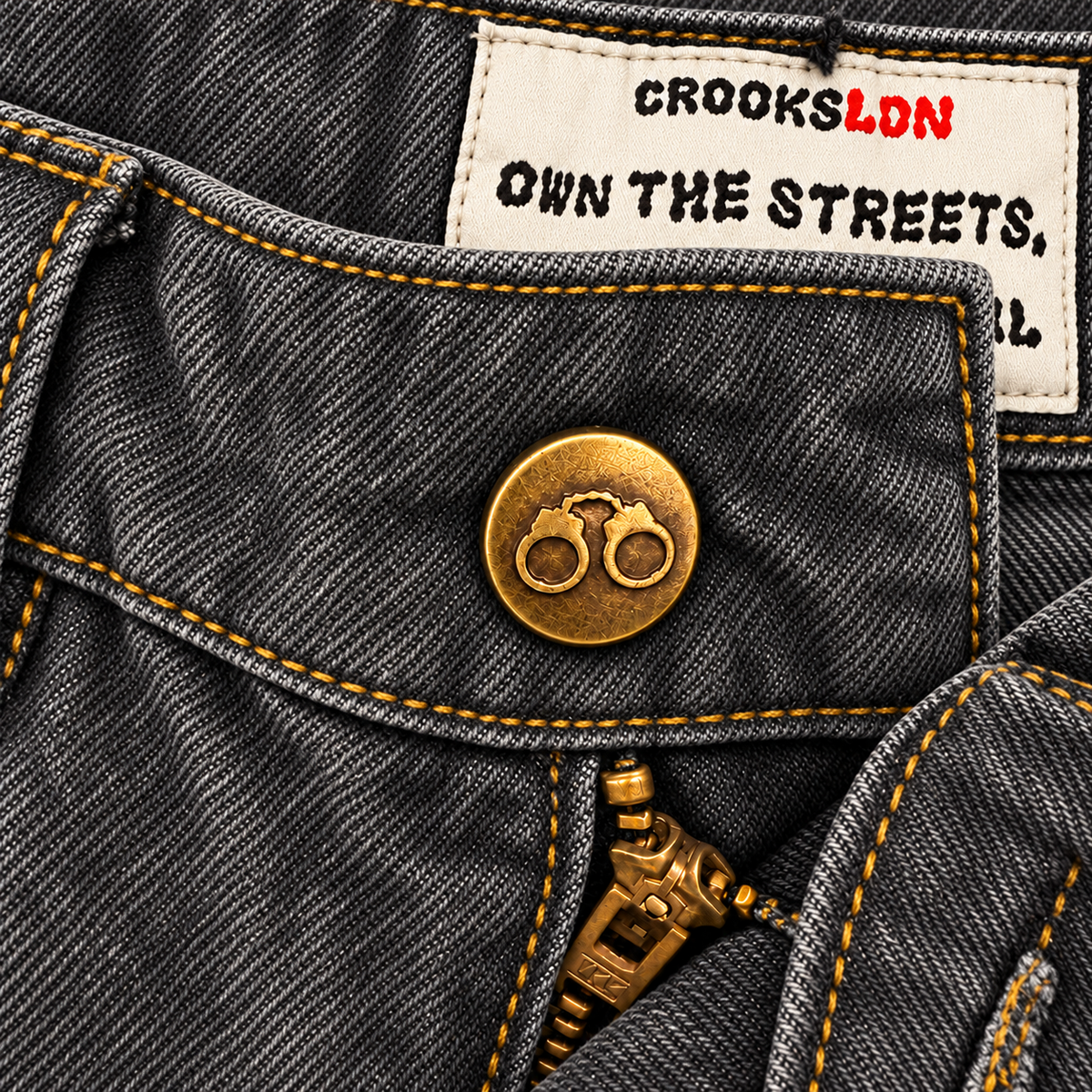CROOKSLDN Grey Wash Yard Jeans — brass handcuff button, zipper and inside OWN THE STREETS label.